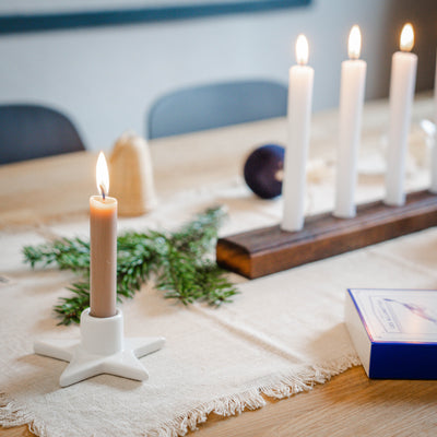 Auf einem dekorierten Tisch liegt einiges an Weihnachtsdekoration. Neben Kerzen steht ein großer, länglicher Kerzenständer aus Holz. 